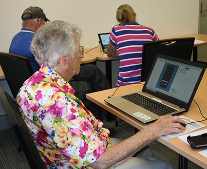 Senior using a computer to learn how to use her mobile phone